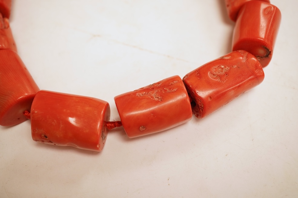 Two coral bead necklaces, one composed of large cylindrical coral beads, approximately 2.5-3.5cm each, total length 49cm; and a bracelet composed of carved coral beads spaced by smaller pink coral beads, on an elasticate